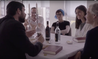 fem personer der sidder rundt om et bord med vinflasker og lysestager