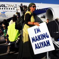 En kvinde ude foran et EL-AL fly med et skilt hvorpå der står 'I'm making Aliyah'